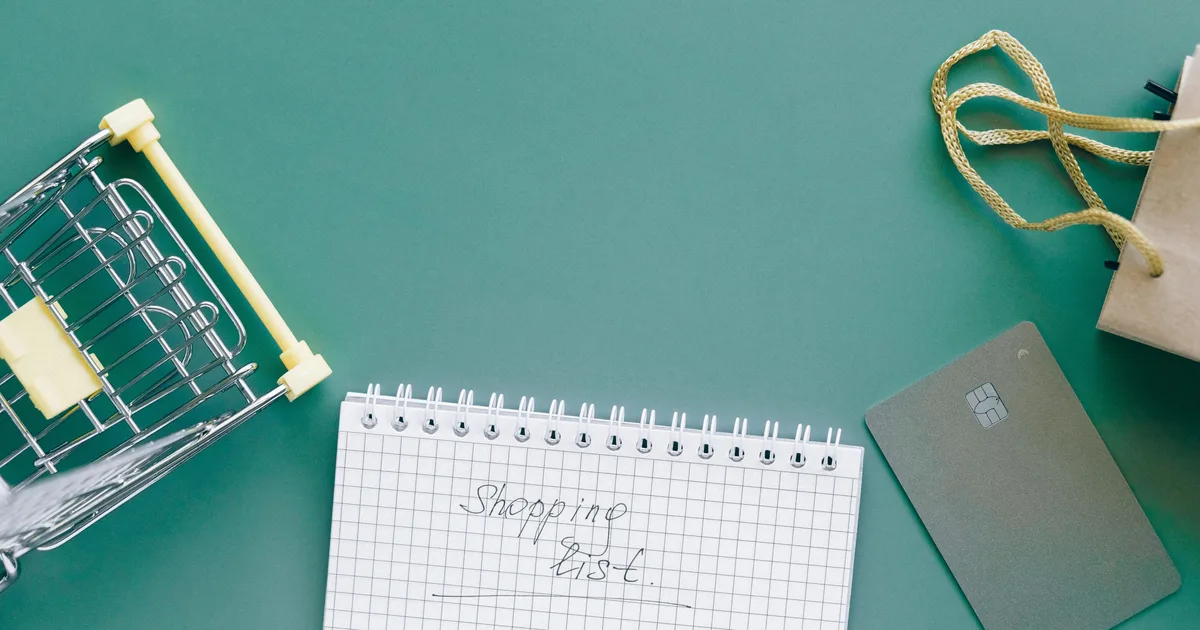 Shopping list, small cart, and payment card on a green background for grocery budget planning